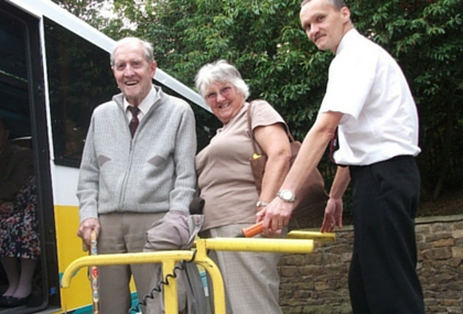 Two older people are lifted onto a bus for a day trip
