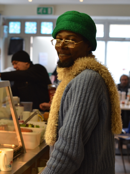 A man in a green hat and woolly scarf serves himself from a canteen
