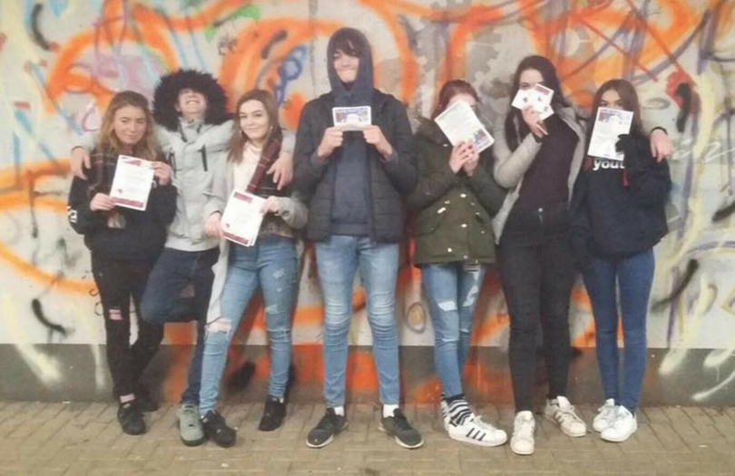 Young people lined up against a graffiti wall holding certificates