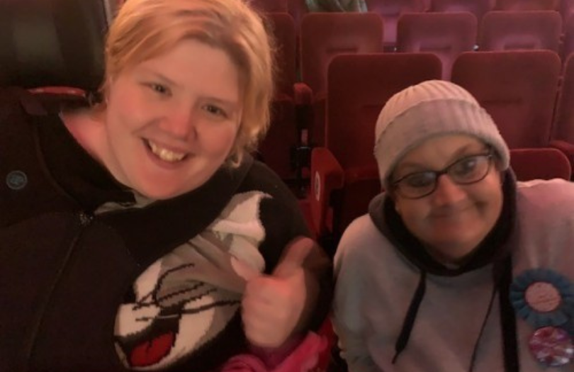 Community Capacity News Image 810×525 Two people, smiling and sitting together in a theatre.