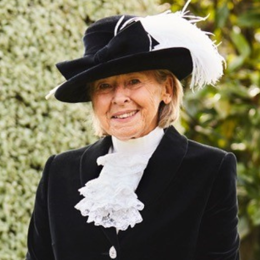 Sally Scott, the new High Sheriff of Oxfordshire, is smiling and wearing her ceremonial uniform which consists of a black velvet coat, white shirt with lace ruffles and a black hat with white feathers.