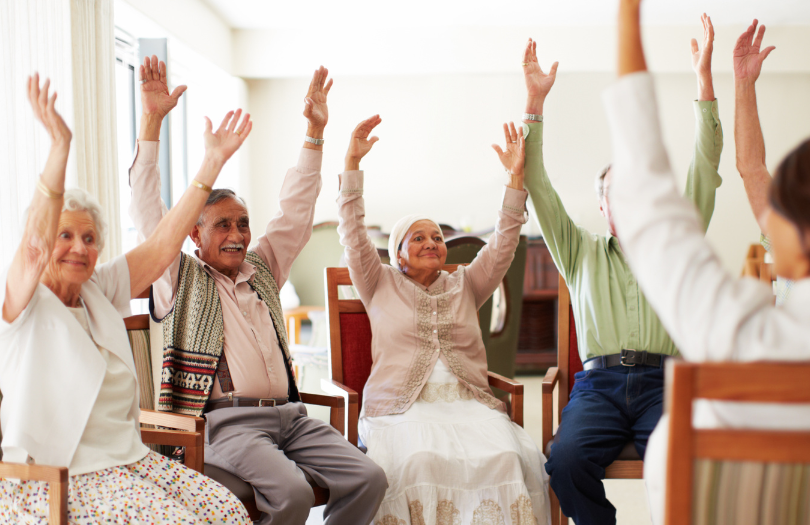 Community Capacity header (3) A group of elderly people taking part in a seated exercise class.