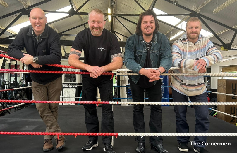 The Cornermen 810×525 Four smiling men in a boxing ring with caption: "The Cornermen"