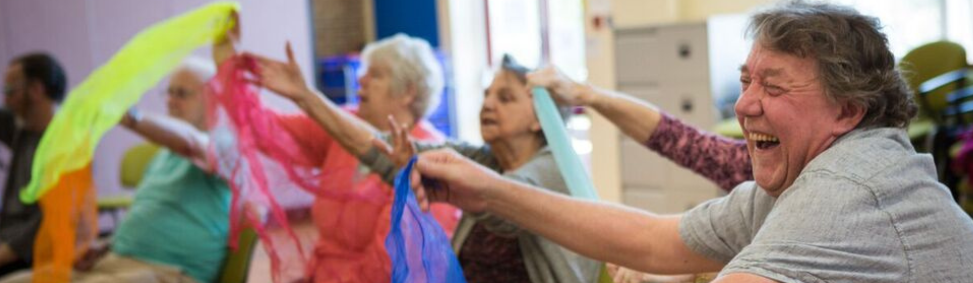 Elderly people sitting down and waving coloured scarves.