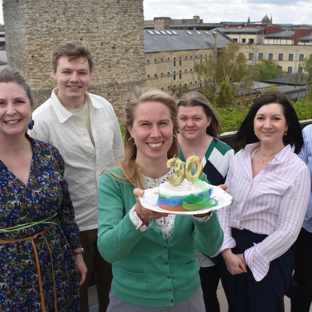30th birthday news story 810×525 6 of the OCF team standing outside and holding a 30th birthday cake and balloons.