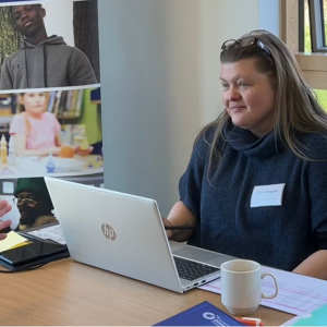 A woman sitting in front of a laptop chatting to another woman across the desk.