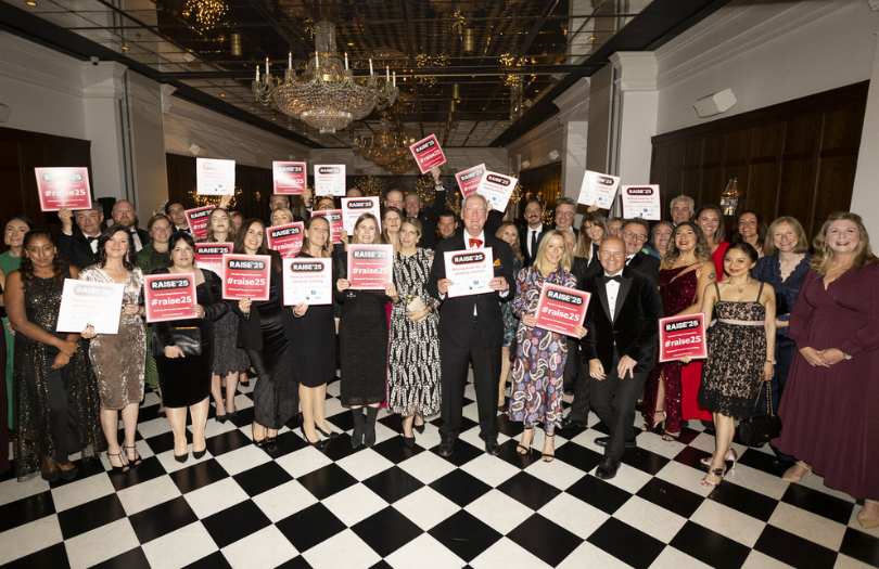 B4 Raise match news story 810×525 Group of guests in the Randolph ballroom holding up Raise'25 signs