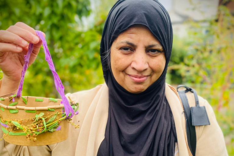 Thriving in Nature news story 810×525 Lady standing in garden holding a basket decorated with flowers.