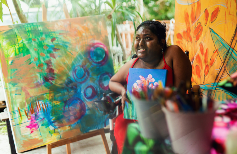 Young female person sitting in a wheelchair and painting a picture in an art studio.