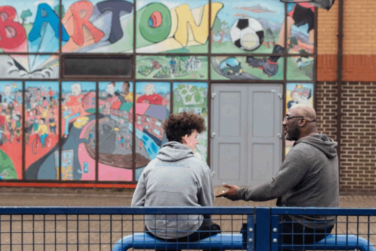 LEF news story image 810×525 An older black man talks supportively to a younger white man in front a of mural in Barton, Oxford