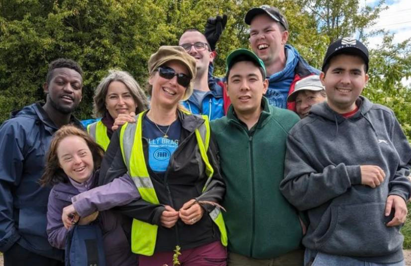 A group of nine happy people standing outside by a tree.