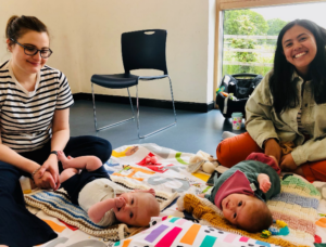 Two women sitting on the floor with a baby in front of each.