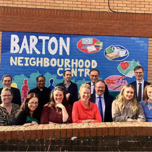 A group of people standing in front of a mural saying 'Barton Neighbourhood Centre' and smiling.