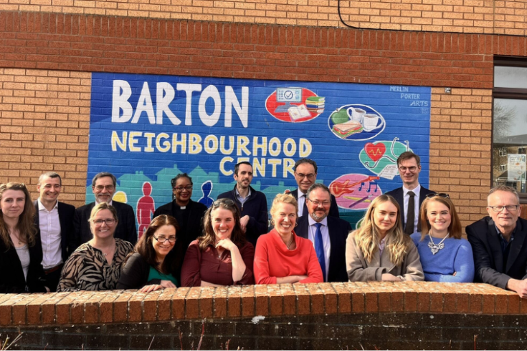 A group of people standing in front of a mural saying 'Barton Neighbourhood Centre' and smiling.