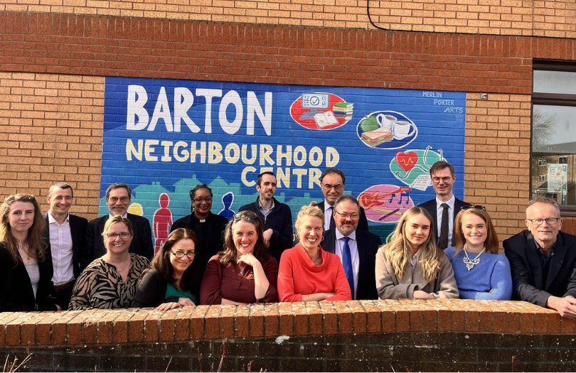 A group of people standing in front of a mural saying 'Barton Neighbourhood Centre' and smiling.