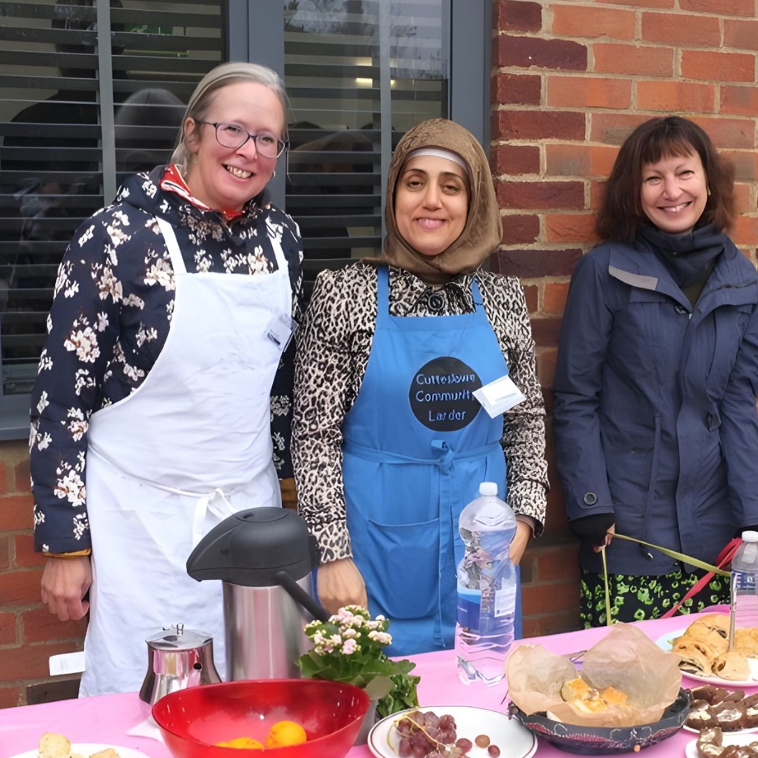 Three ladies with aprons on, standing behind a table and serving food.
