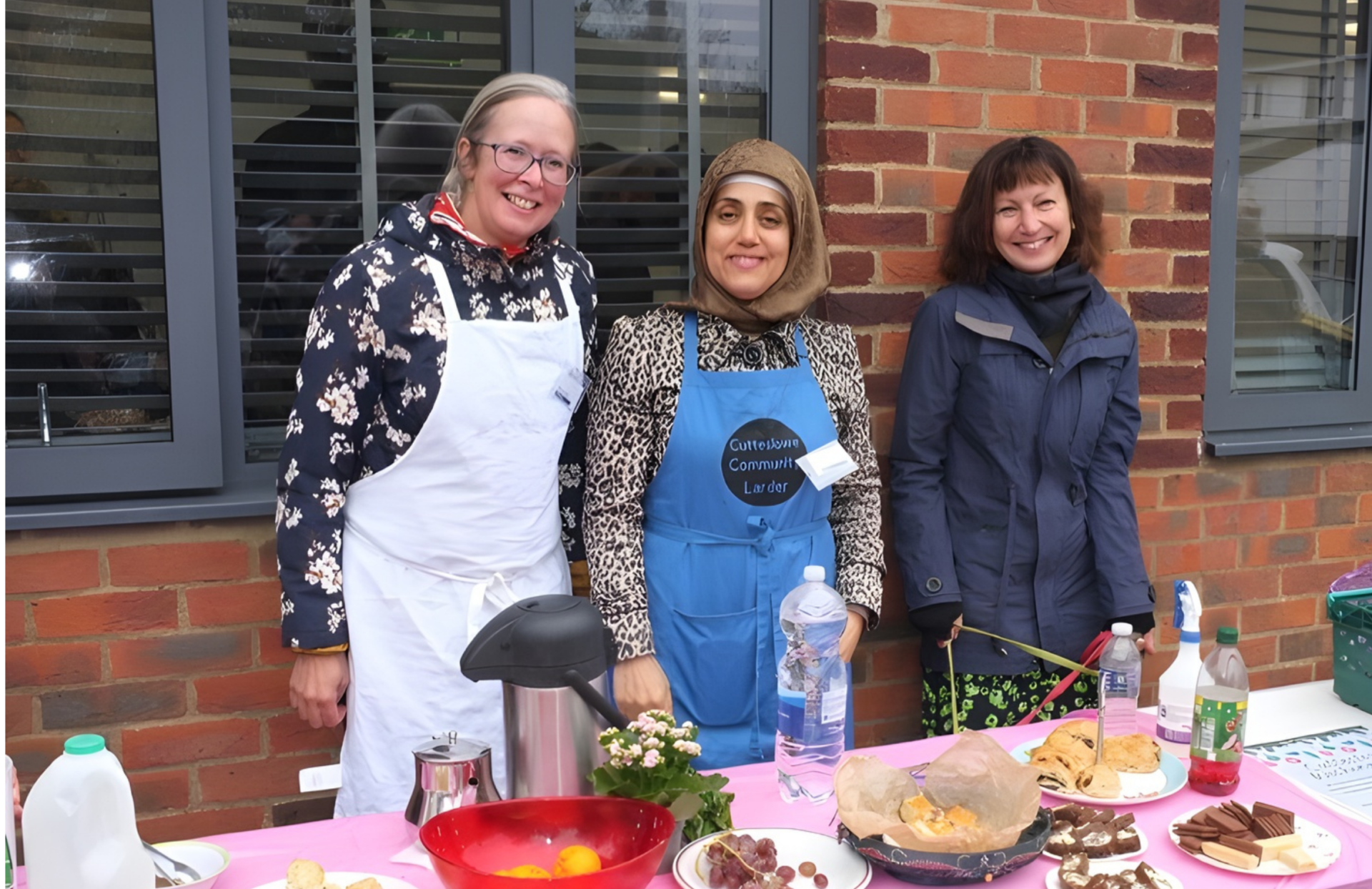 Three ladies with aprons on, standing behind a table and serving food.