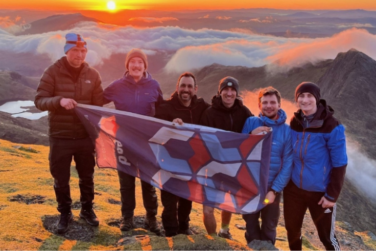 Beard news story Jul 26 810×525 Six people at the top of Snowdon holding a Beard Construction flag with the sun rising behind them.