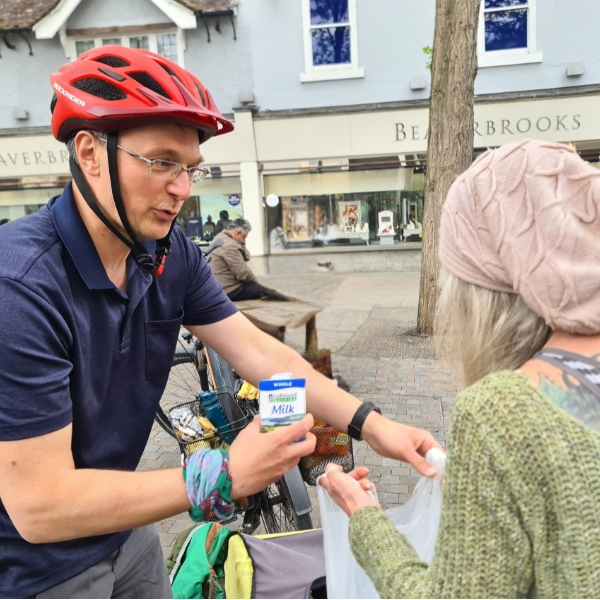 Man on a bike putting a carton of milk into a persons bag.