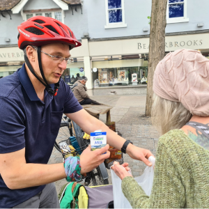 Man with a bicycle filling up a persons bag with milk and other food items.